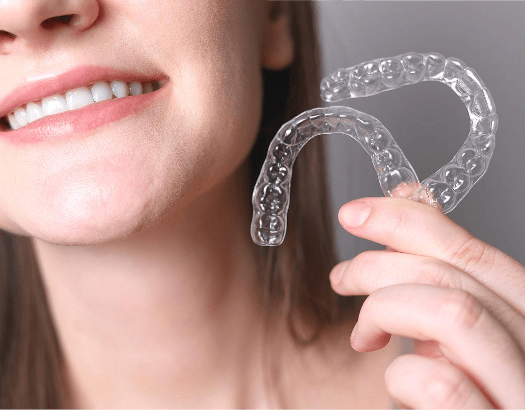 A patient holding a clear Invisalign<sup>&reg;</sup> aligner and smiling at Dentistry at Millennium Park in Chicago