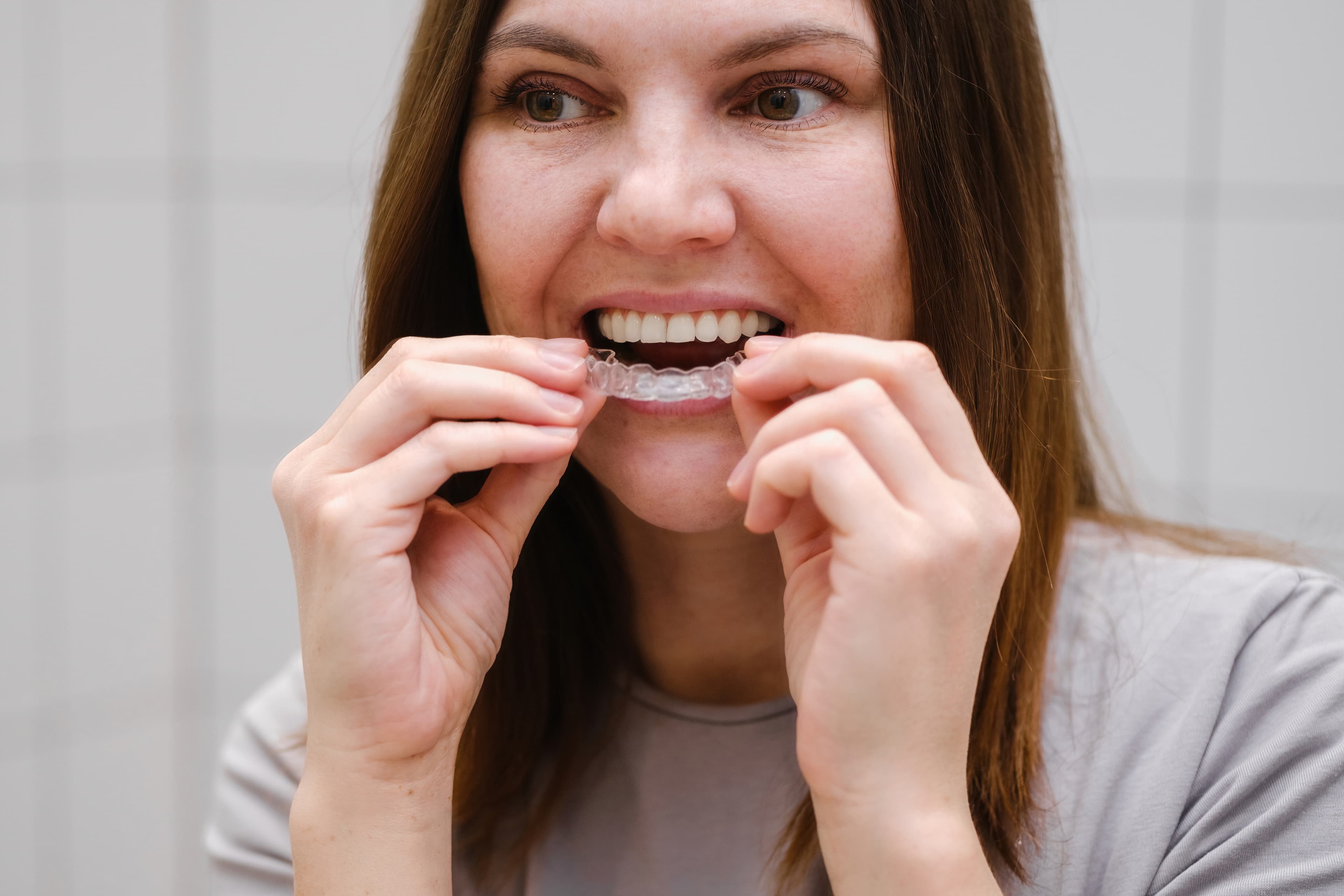 A woman placing a clear aligner in her mouth